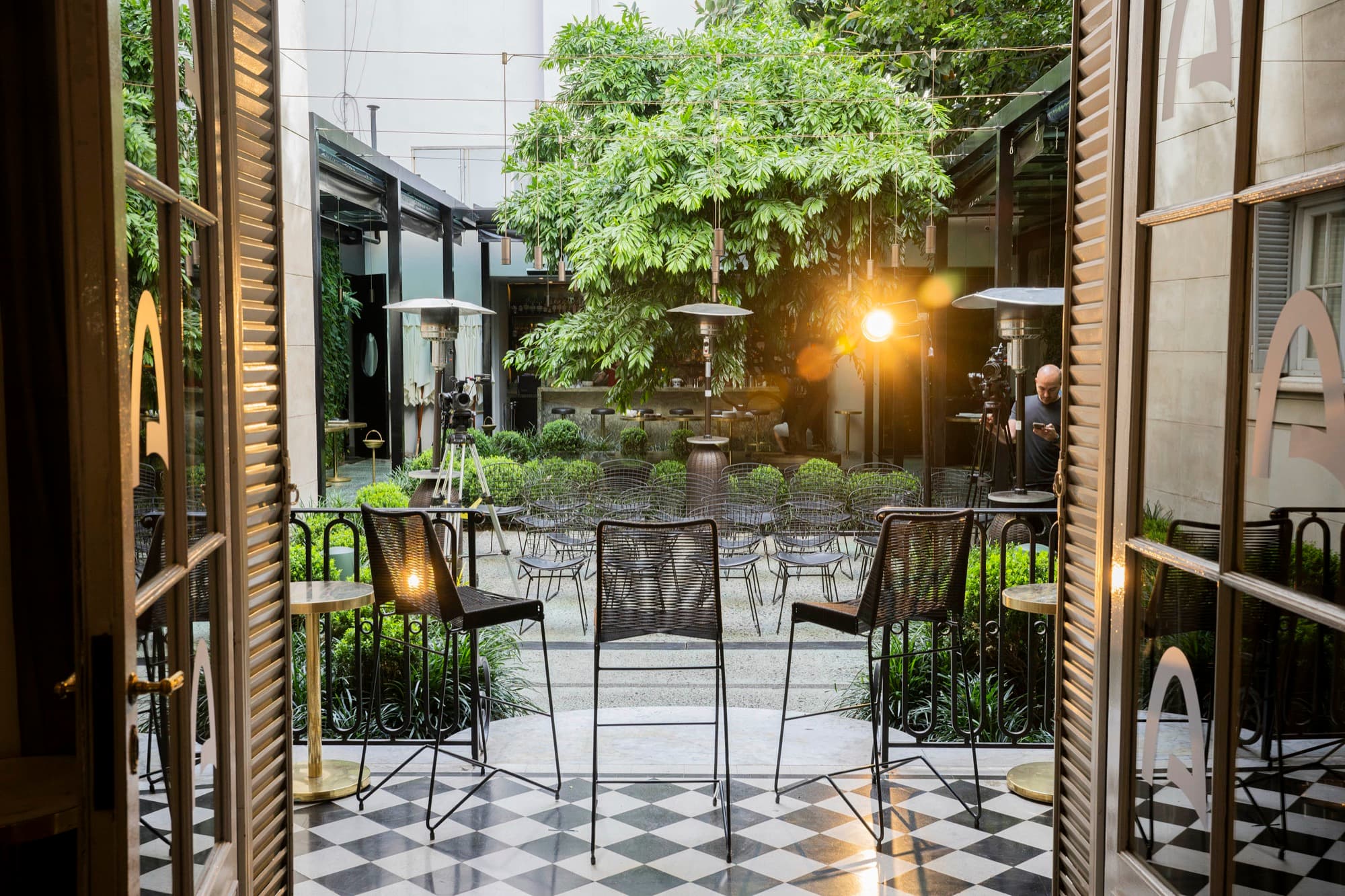 Tall glass doors open onto a checkered courtyard set with bar tables