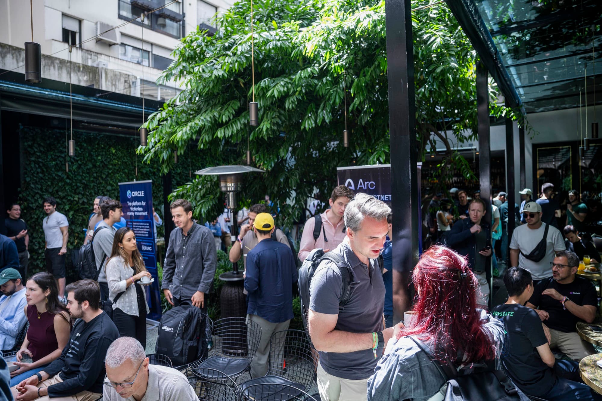 Attendees mingling in a leafy glass-roofed courtyard at an Arc event